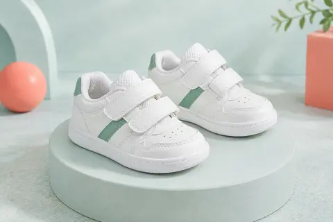 Baskets bébé Adidas Advantage blanches à détails verts, posées seules sur un socle mat bleu brume.