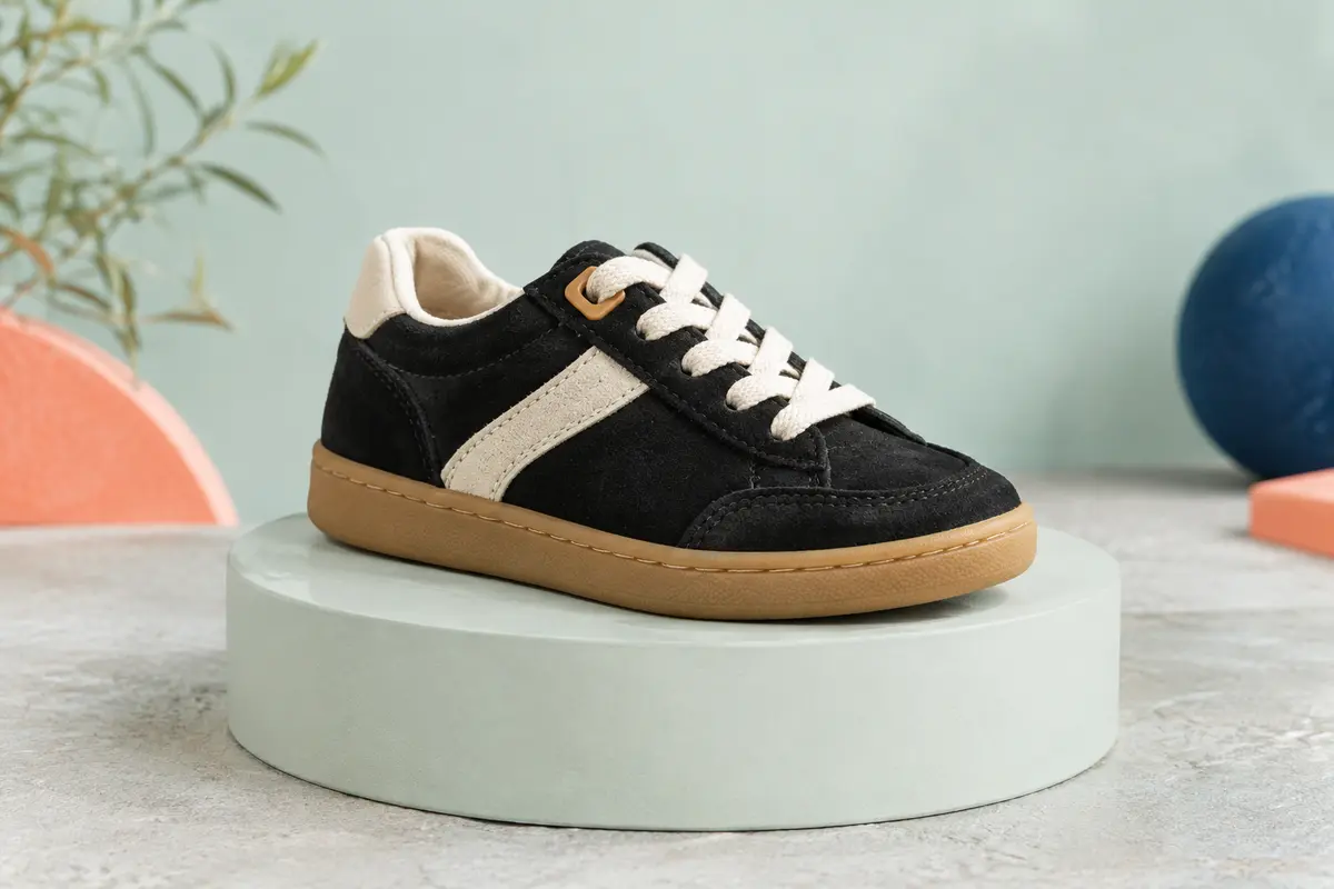 Basket basse enfant en cuir suédé noir avec détails clairs, présentée seule sur un fond vert d’eau pâle.