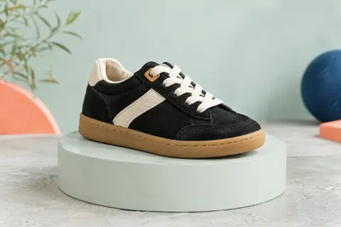 Basket basse enfant en cuir suédé noir avec détails clairs, présentée seule sur un fond vert d’eau pâle.