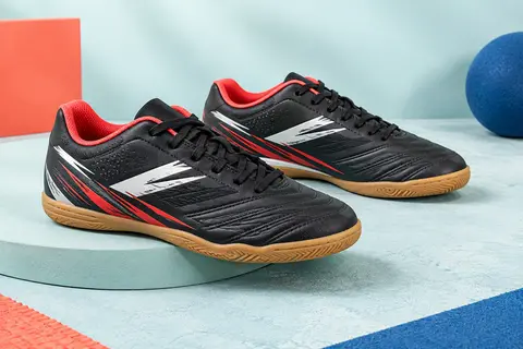 Paire de chaussures de futsal enfant noires, blanches et rouges, à lacets, posée sur un socle mat.