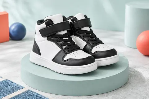Basket montante enfant blanche et noire, avec lacets, scratch et semelle en caoutchouc sur un socle clair.