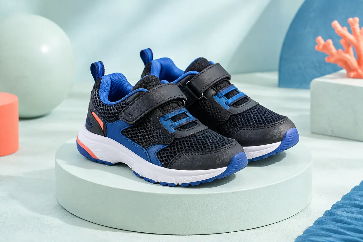 Paire de baskets enfant noires et bleues en mesh, à scratch, présentées sur un socle clair.