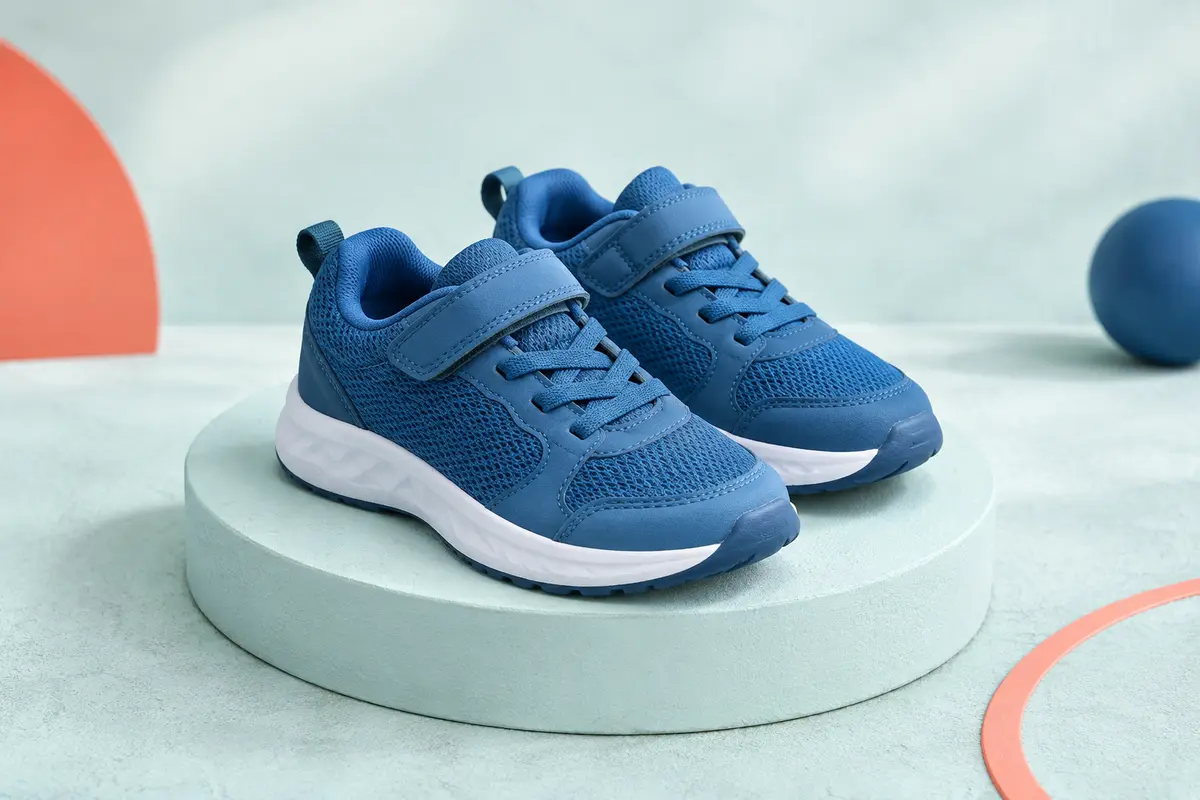 Paire de baskets de sport enfant bleues, basses et respirantes, présentées sur un socle mat clair.