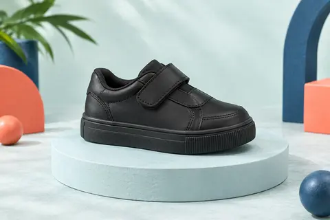 Basket basse noire pour enfant à fermeture scratch, posée seule sur un socle mat dans un décor clair.