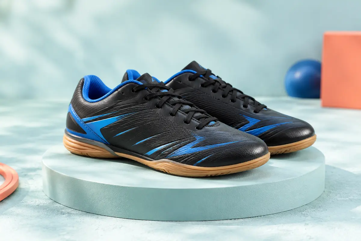 Paire de chaussures de football en salle pour enfant, en matière synthétique noire et bleue.