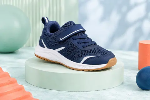 Basket basse enfant bleue en maille avec détails blancs et semelle en caoutchouc, posée sur un socle clair.
