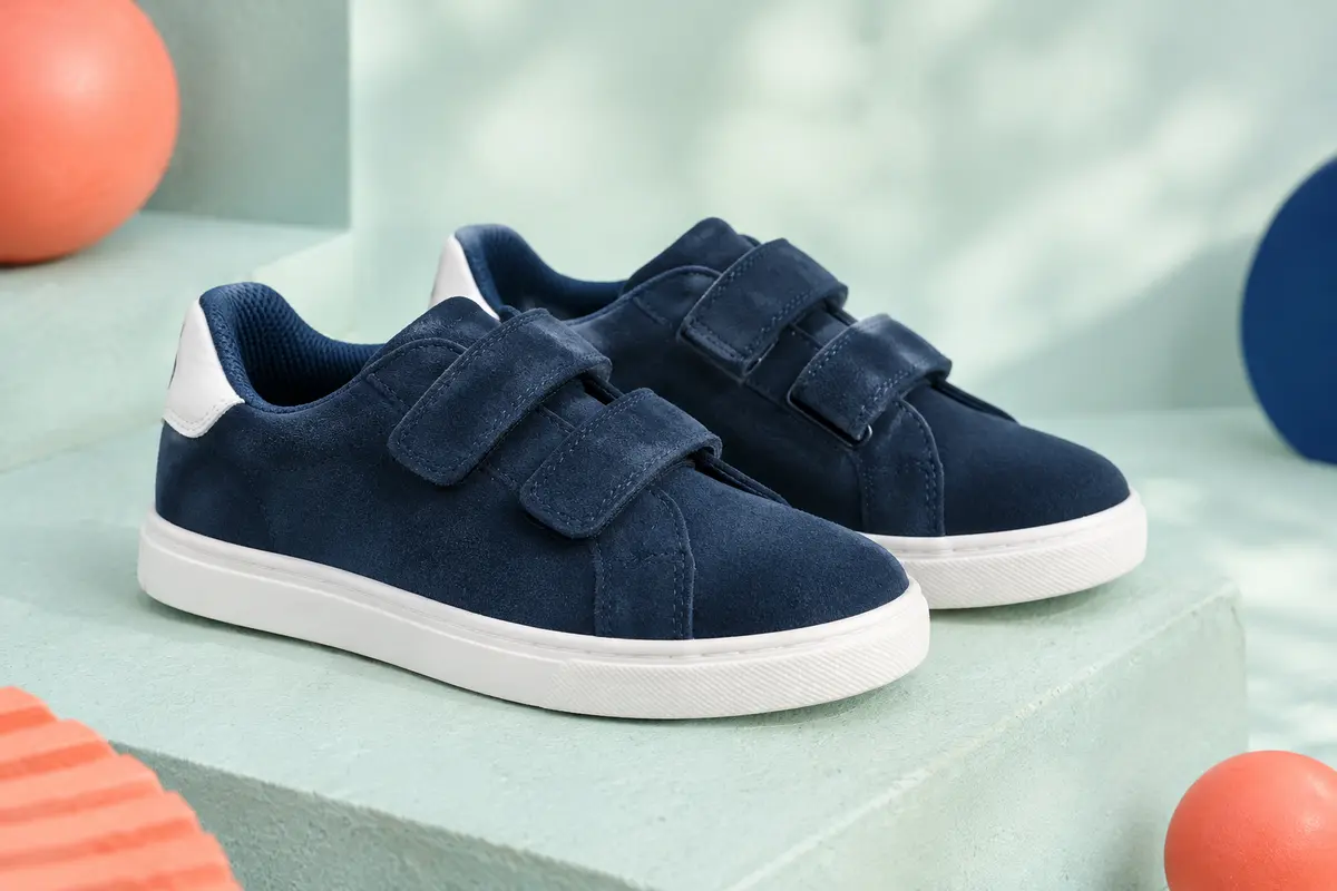 Paire de baskets basses enfant en daim bleu marine à fermeture autoagrippante et semelle blanche, posée sur un socle mat.