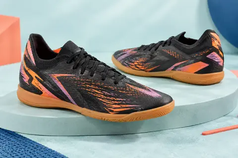 Paire de chaussures de futsal junior Puma Future 8 Play, noire avec des accents orange et rose, sur un socle mat.