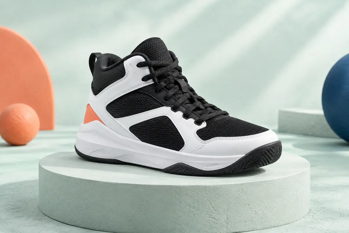 Chaussure de basket junior noire et blanche en maille, posée sur un socle mat vert d’eau