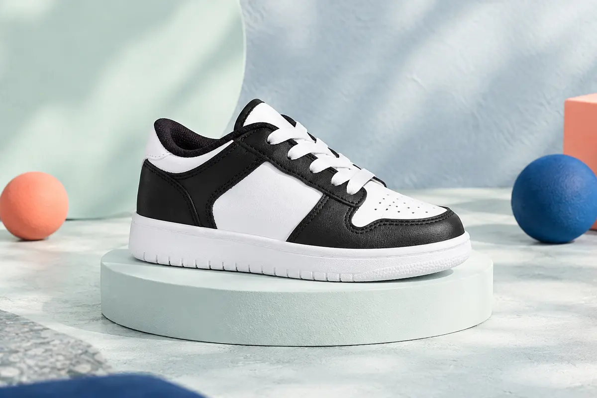 Basket basse pour enfant en cuir noir et blanc, posée sur un socle mat dans un décor lumineux