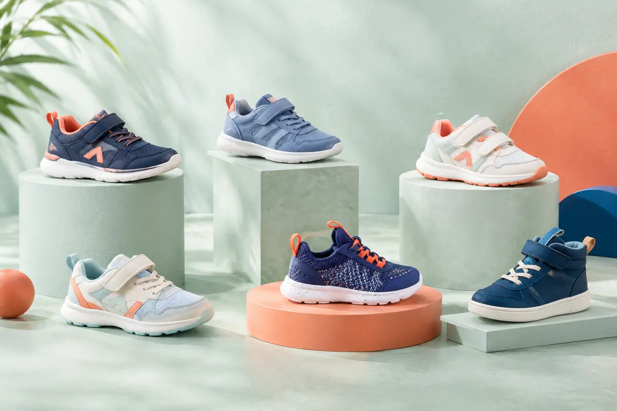 Baskets pour enfants présentées seules dans une composition lumineuse aux accents corail et bleu profond